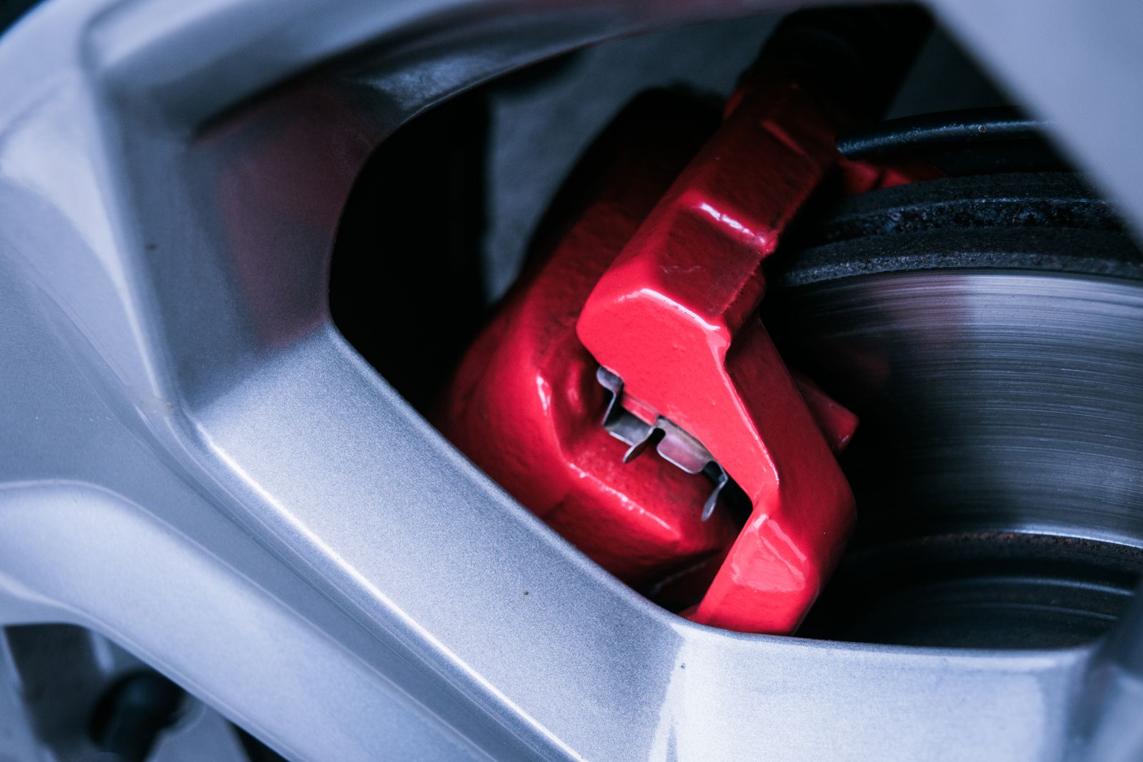 A red-painted brake caliper and disc seen through the spokes of a silver alloy wheel