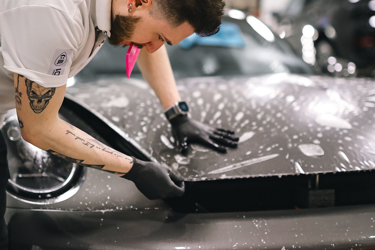Clear paint protection film being squeegeed onto a car bonnet