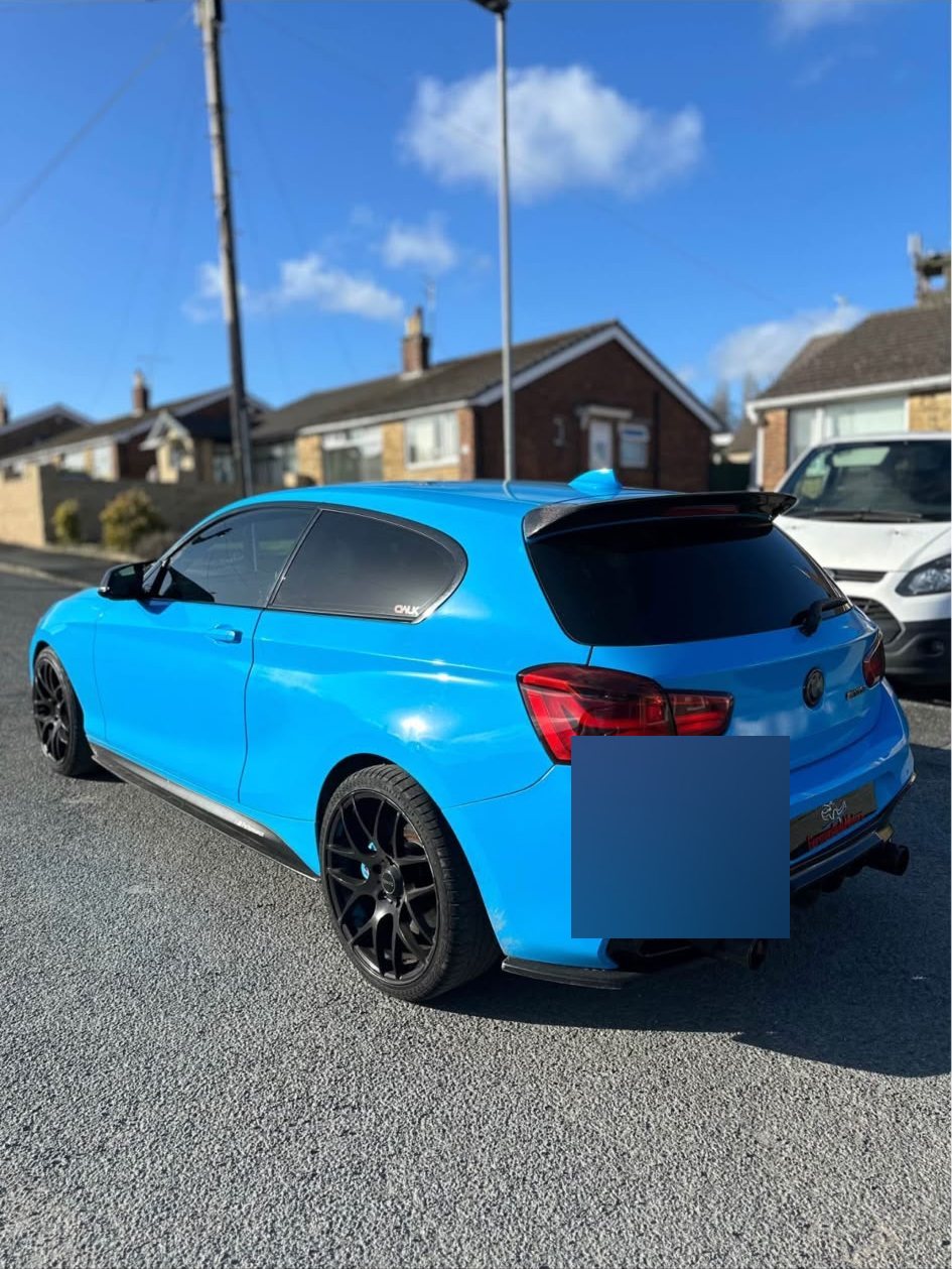 Rear three-quarter of the gloss blue BMW 1 Series with a roof spoiler